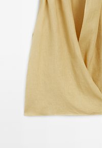 Hellgelber Leinenstoff mit weicher Textur, der mit einem V-Ausschnitt und einem lockeren Schnitt drapiert ist, ideal zum Layering.