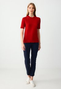 Rode gebreide top met korte mouwen en een ronde hals, gecombineerd met strakke marineblauwe broek en witte sneakers. Glad textuur, eenvoudig ontwerp.