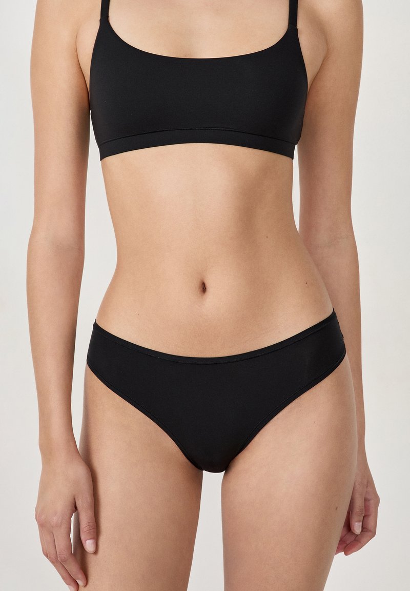 Czarny biustonosz bikini z dekoltem w serek i cienkimi ramiączkami, w połączeniu z dopasowanymi, niskimi majtkami bikini, o gładkim, matowym wykończeniu.