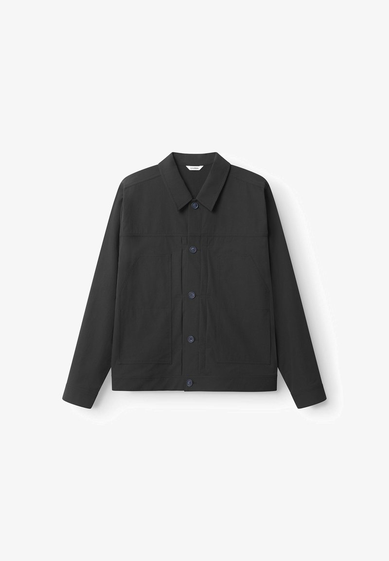 Veste noire en tissu à texture lisse. Dotée d'un col pointu, de manches longues, d'une fermeture à boutons sur le devant et de deux grandes poches avant.