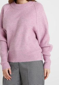 Suéter de punto rosa claro con textura acanalada, cuello redondo y hombros caídos. Combinado con pantalones de patrón de pata de gallo en blanco y negro.