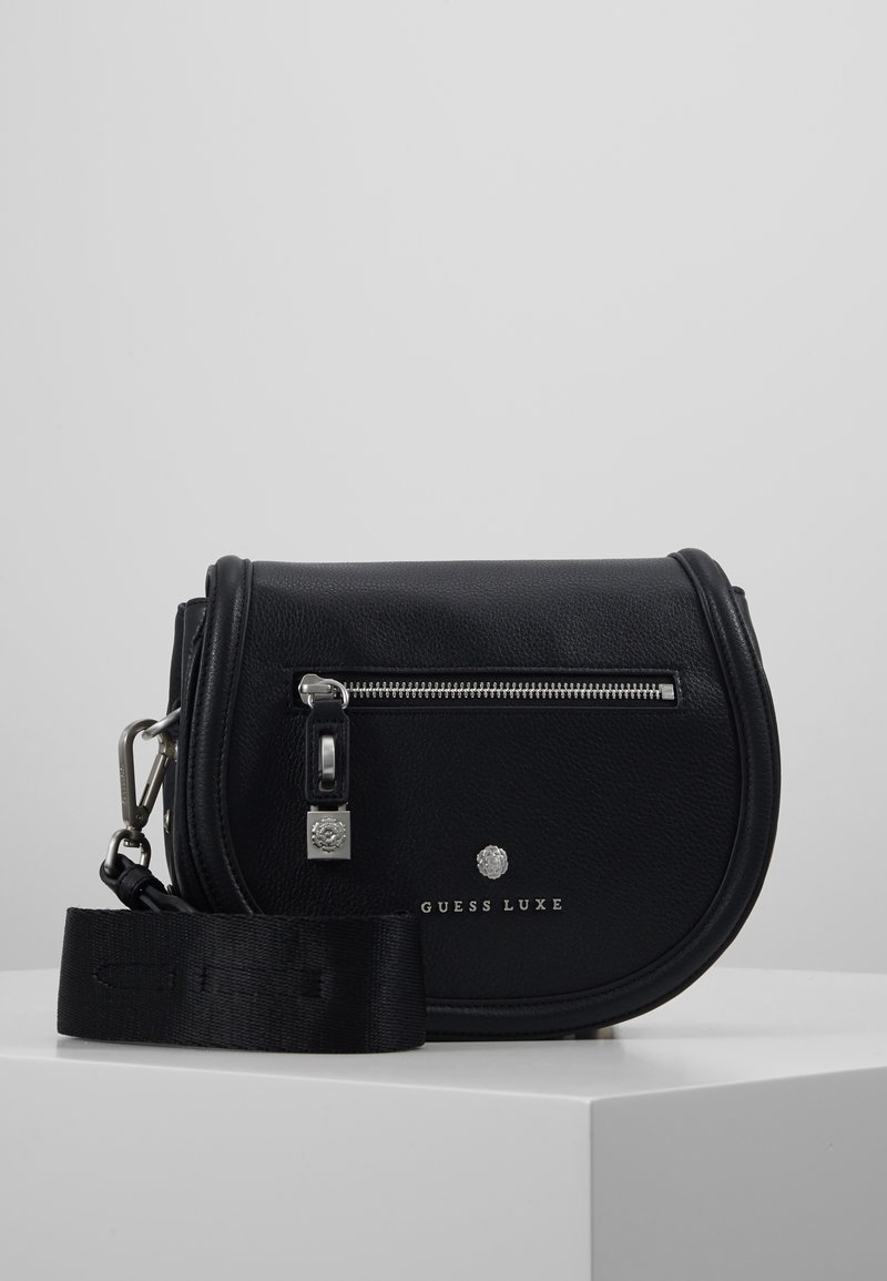 Černá kožená crossbody taška zaobleného tvaru, se stříbrnými kovovými doplňky, zipovým uzávěrem, s logem na přední straně a nastavitelným textilním popruhem.