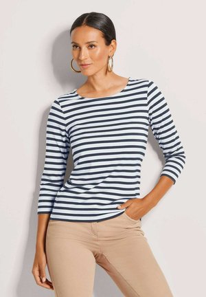 Gestreepte langemouwen top met marineblauwe en lichtblauwe horizontale strepen. Ronde halslijn, zachte stof, gecombineerd met beige aansluitende broeken.