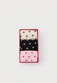 Trei perechi de șosete pliate cu modele cu inimioare în culori bej, negru și roz, aranjate într-o cutie dreptunghiulară roșie pe un fundal alb.