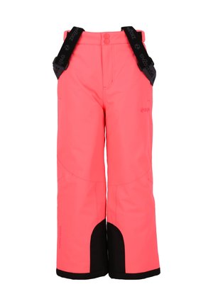 Niño con pantalones de nieve rosa brillante con tirantes negros y camisa negra de manga larga, de pie con las manos entrelazadas contra un fondo blanco.