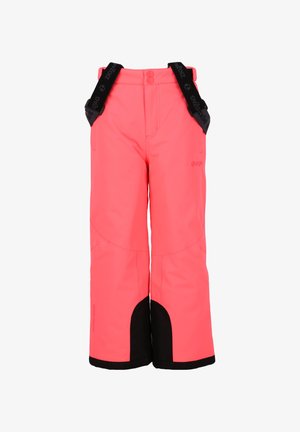 Niño con pantalones de nieve rosa brillante con tirantes negros y camisa negra de manga larga, de pie con las manos entrelazadas contra un fondo blanco.