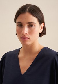 Top blu navy a maniche corte con scollatura a V e leggeri arricciamenti sulle spalle, realizzato in un tessuto liscio e leggero.