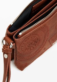 Pochette en cuir brun avec des motifs en relief en forme de rayon de soleil, fermeture éclair argentée, surface texturée et une sangle pour le poignet.