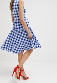 Blau-weiß kariertes Kleid mit tailliertem Oberteil und schwingendem Rock, kombiniert mit roten High Heels mit Knöchellriehmen.