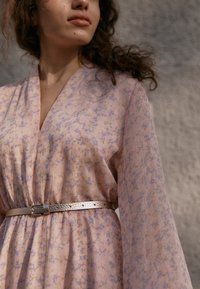 Robe à motifs floraux de couleur rose clair avec des accents violets, dotée d'un décolleté en V et de manches longues, cintrée par une ceinture en métal argenté.
