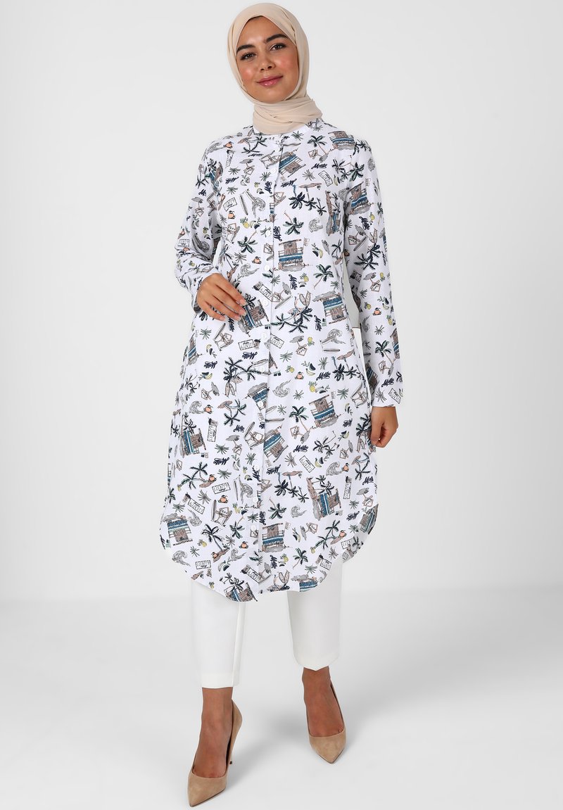 Witte tuniek met lange mouwen, voorzien van een kleurrijke print van tropische bladeren en gebouwen. Afgeronde zoom en knoopsluiting met een casual pasvorm.