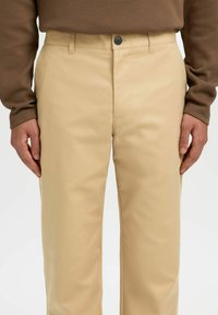 Beige, raka byxor i bomullsblandning. Har knappstängning, sidofickor och en slät yta.