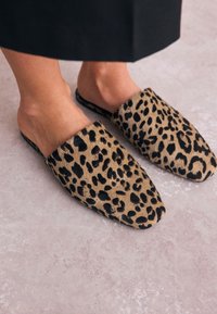 Mules à enfiler à imprimé léopard avec une surface douce et texturée et un design à bout pointu, présentant un schéma de couleurs beige et noir.