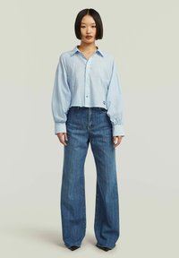 Camicia button-up azzurra chiara a maniche lunghe e voluminose, abbinata a jeans in denim blu a gamba larga con vita alta.