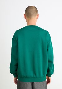 Sweatshirt verde com decote redondo, mangas longas e um ajuste relaxado. Apresenta punhos e bainha canelados, feito de um material de algodão suave.