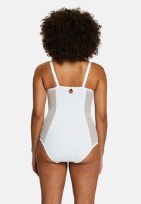 Maillot de bain blanc en une pièce avec bretelles réglables, une découpe en forme de clé dans le dos et des panneaux latéraux transparents, présentant des bords à volants.