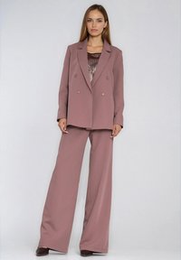 Dwurzędowa marynarka w kolorze różu brzoskwiniowego z dużymi guzikami, zestawiona z szerokimi spodniami w tym samym odcieniu. Pod spodem teksturowany sweter.