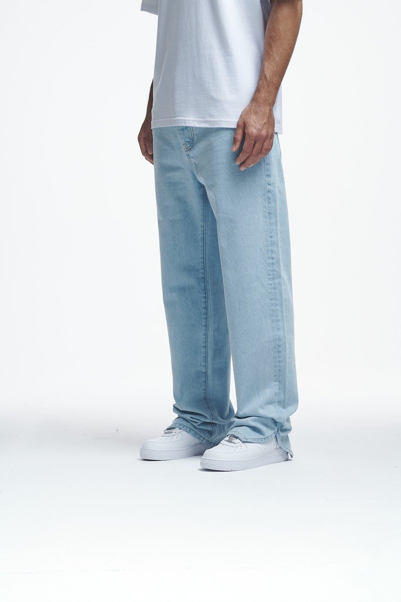 Jean en denim bleu clair avec une coupe décontractée, porté avec un t-shirt gris ample et des baskets blanches, présentant un design simple sans motifs visibles.