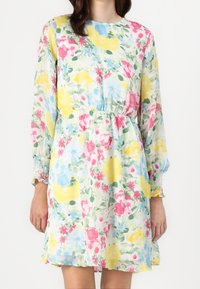 Robe fleurie en tissu léger et texturé avec manches longues, poignets élastiques et taille élastique, présentant des fleurs roses, jaunes et bleues.