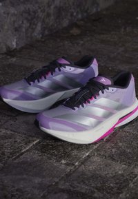 Lekkie buty biegowe w odcieniach fioletu z srebrnymi akcentami, siateczkowa cholewka oraz amortyzowana biała podeszwa z różowymi detalami.