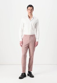 Chemise blanche ajustée, pantalon texturé rose, coupe slim, présentés avec des chaussures en cuir noir sur un fond uni.