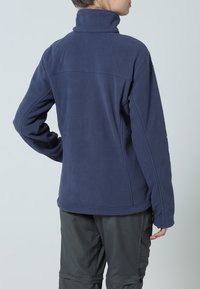 Tummansininen fleece-takki, jossa on korkea kaulus, sileä pinta ja kontrastiväriset ompeleet. Suunnittelussa on muotoiltu istuvuus ja pitkät hihat.
