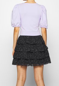 Top de mangas abullonadas en color lila combinado con una falda negra con volantes en capas que presenta un patrón moteado en blanco. Mezcla de algodón, textura suave.