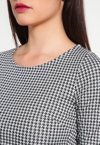 Black and white houndstooth-patterned knit top with a round neckline and soft texture. Focus on fabric details without additional design elements.