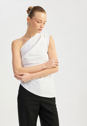 Top bianco asimmetrico realizzato in tessuto texturizzato, con una spalla scoperta, abbinato a pantaloni neri sartoriali.