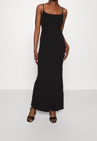 Svart maxiklänning med tunna axelband, åtsittande liv och en lätt utsvängning vid fållen. Bärs med svarta klacksandaler med öppen tå.