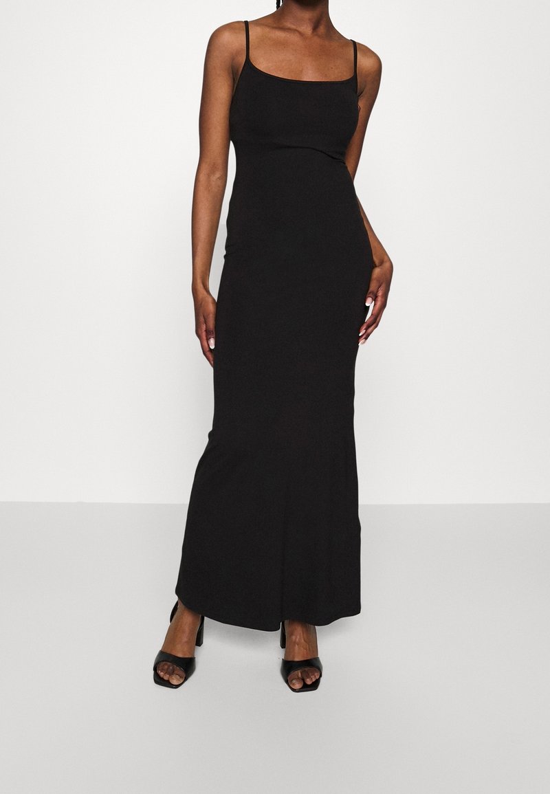 Svart maxiklänning med tunna axelband, åtsittande liv och en lätt utsvängning vid fållen. Bärs med svarta klacksandaler med öppen tå.
