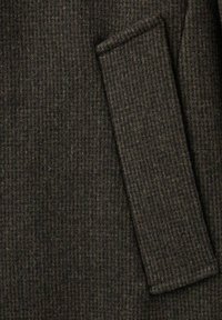 Tela de lana texturizada en marrón oscuro con un sutil patrón de cuadros. Presenta un bolsillo cosido y costuras texturizadas para mayor detalle.