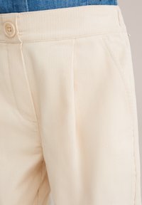 Lichtbeige corduroy broek met een gladde textuur, voorzien van een enkele knoopsluiting en zijzakken. Subtiel verticaal ribbelpatroon.