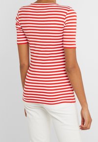 Top de manga corta a rayas rojas y blancas, diseño ajustado, cuello redondo, tela de algodón suave, costuras del dobladillo visibles, combinado con pantalones blancos.