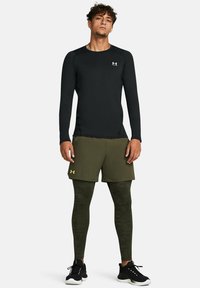 Long-sleeve black athletic top with logo, green shorts, and textured green leggings. Worn with black athletic shoes.