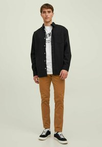 Black button-up shirt over a white graphic T-shirt, paired with tan pants and black sneakers. Simple design, casual style, slight texture.