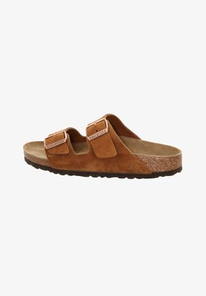 Brown suede sandal with two adjustable straps, light brown footbed, and dark textured sole. Features metallic buckles with brand name.