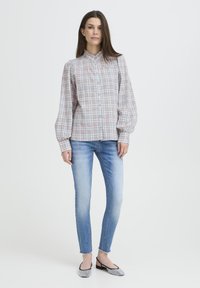 Karierte Hemdjacke mit Stehkragen, gefertigt aus weichem, strukturiertem Stoff in hellen Farben mit Mustern in Blau, Rosa und Beige. Kombiniert mit engen Jeans.