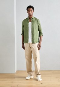 Cămașă din in verde, cu nasturi, purtată peste un maiou alb, asortată cu pantaloni bej și adidași albi. Material neted cu mâneci răsfrânte.