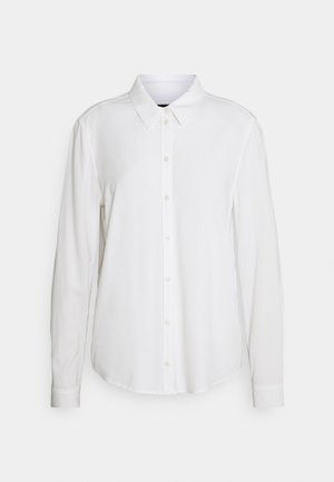 Chemise blanche à manches longues en tissu lisse, dotée d'un col pointu, d'une patte de boutonnage à l'avant, et de poignets boutonnés. Design uni sans motifs.