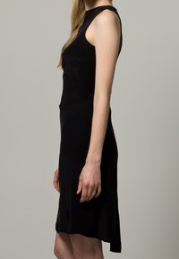 Svart ärmlös klänning i slät tyg, figurnära design, slutar ovanför knäet med minimala sidsömsdetaljer och en enkel silhuett.