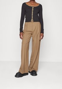 Svart långärmad topp med leopardmönstrade detaljer, i kombination med tanfärgade högmidjade byxor med vida ben och svarta vävda slipskor.