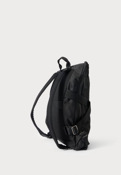 Sac à dos noir élégant avec dos rembourré, bretelles réglables, poche latérale zippée et poignée de transport supérieure, présenté de côté sur fond blanc.