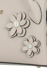 Beige Lederhandtasche mit zwei geschichteten Blumenapplikationen mit Perlenmitten und schwarzen Umrandungen; verziert mit goldfarbenen Beschlägen.