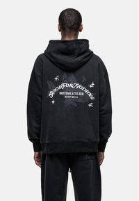 Felpa nera oversize in cotone, con stampa grafica contenente testo e farfalle sul retro, e cappuccio con cordino.