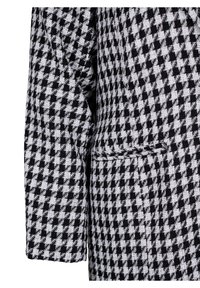 Tejido de patrón houndstooth en blanco y negro. Diseño ajustado con un ligero brillo y hombros estructurados. Cuenta con un único bolsillo discreto.