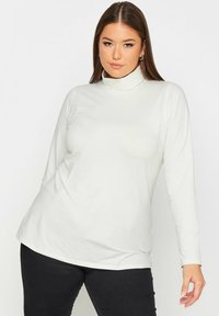 Vit långärmad polotröja i mjukt tyg, med en figurnära design och en slät yta, matchad med mörka byxor.