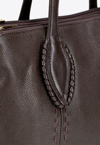 Sac à main en cuir brun avec une finition texturée, mettant en avant des accents tressés sur la poignée et des détails de couture visibles dans une couleur contrastante.