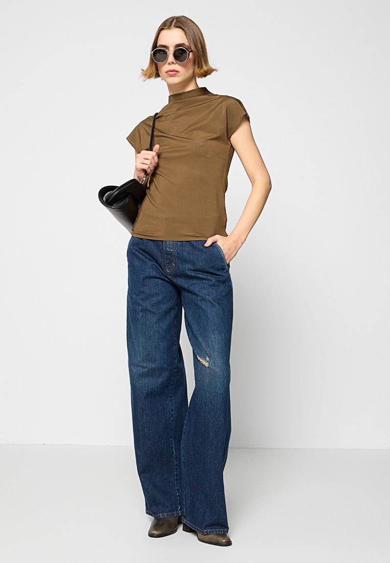 Brązowa, krótki rękaw koszulka z wysokim kołnierzem; zestawiona z szerokimi, zniszczonymi niebieskimi dżinsami oraz czarną torebką; okrągłe okulary przeciwsłoneczne.