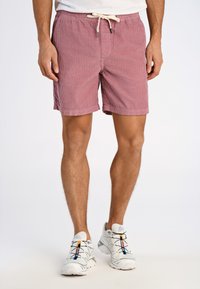 Pantaloni da bagno a righe rosse con elastico in vita e cordoncino. Indossati con sneaker di colore chiaro con lacci multicolori.
